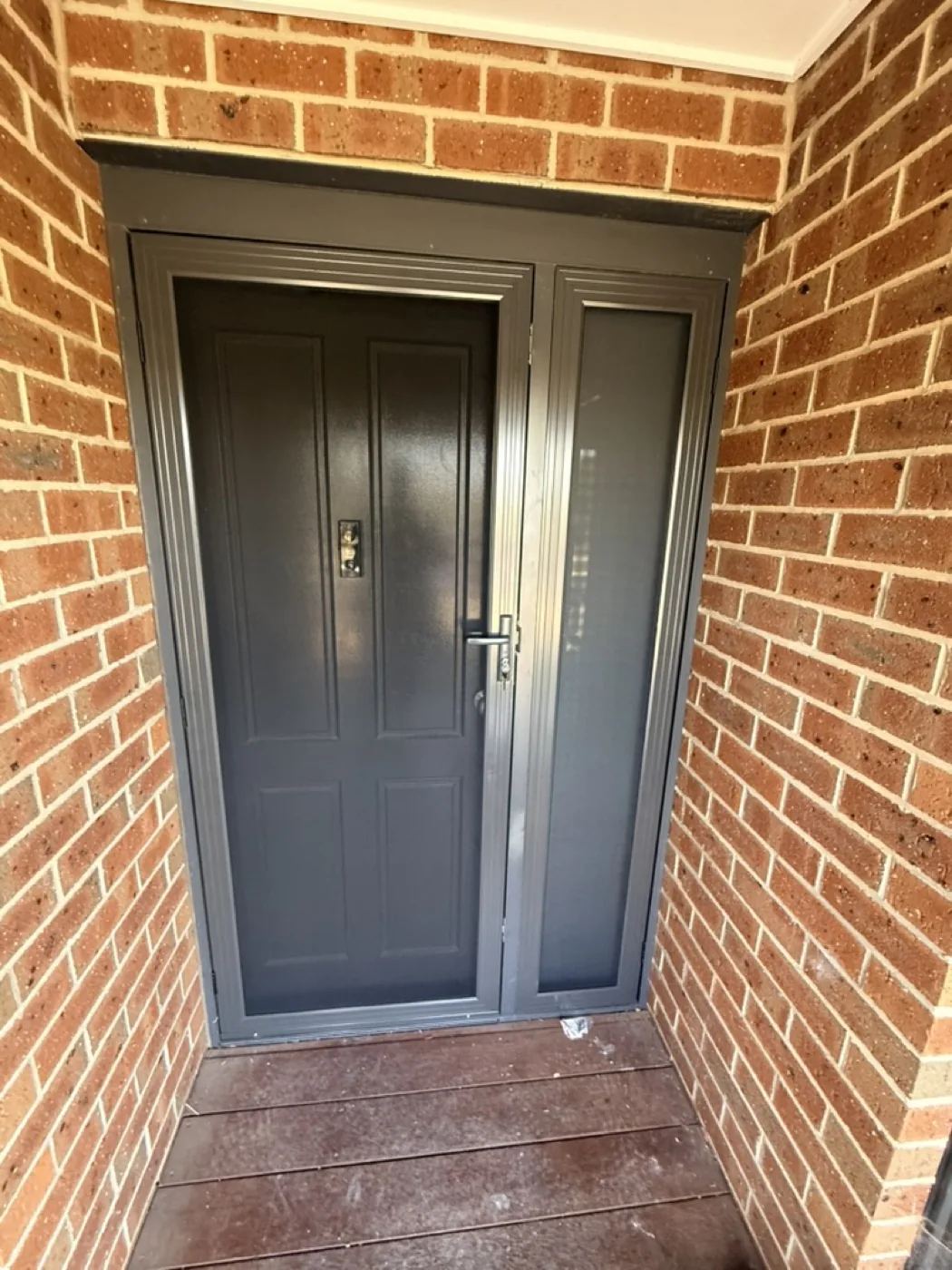 Twin-panel grey security door with mesh sidelight on brick entrance