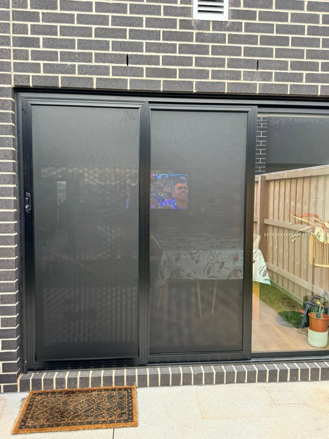 Black triple-track sliding security doors on a bluestone brick home