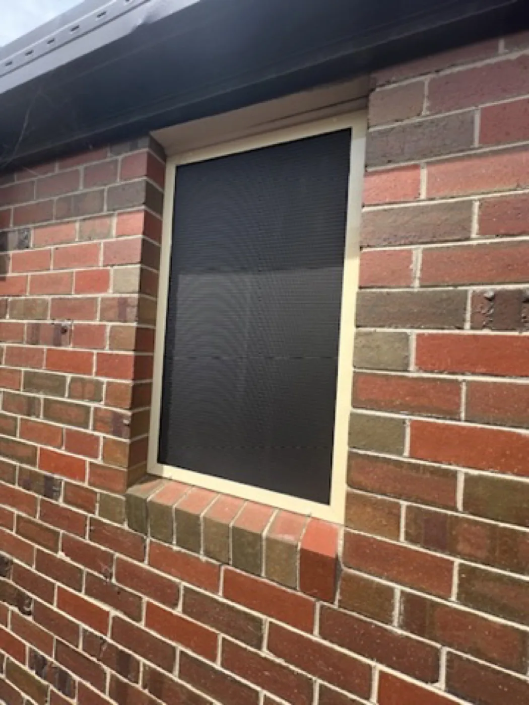 Cream-framed mesh window security screen on heritage red brick