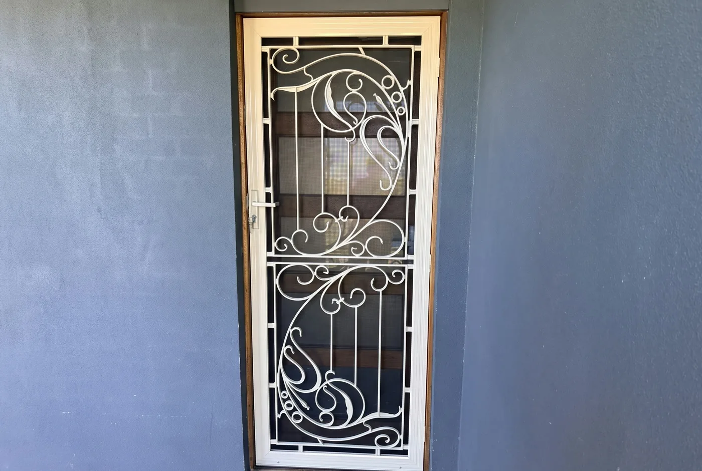 White wrought-iron scroll security door on a charcoal rendered Melbourne entrance